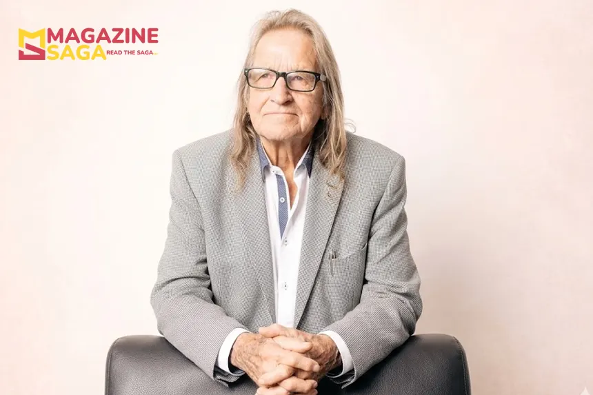 George Jung in 2026, wearing a grey blazer and glasses, seated with hands clasped