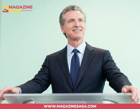 Gavin Newsom standing at a podium in a dark suit, looking upward during a public speaking appearance.