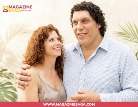 A smiling woman with curly red hair and a tall man with curly dark hair embracing, set against tropical foliage.
