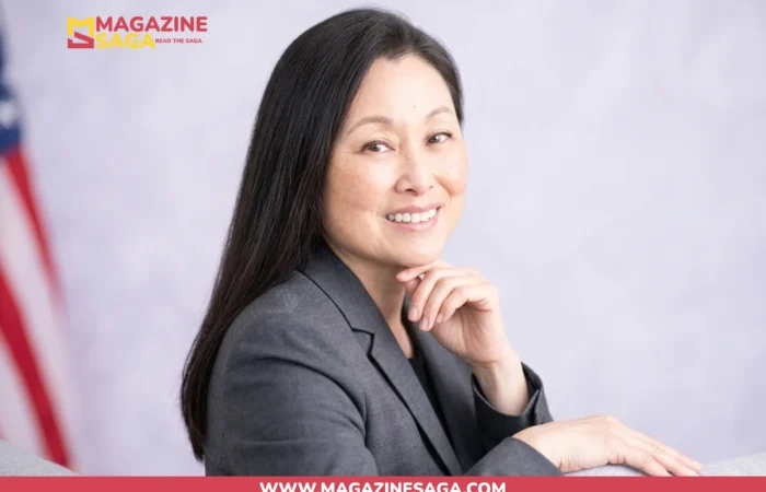 Jennifer Wicks McNamara smiling in a gray blazer with an American flag in the background