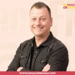 Jimmy Failla smiling with arms crossed, wearing a dark jacket, against a light beige studio background