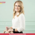 Karen Carney smiling in a white blouse, holding glasses in a professional studio setting