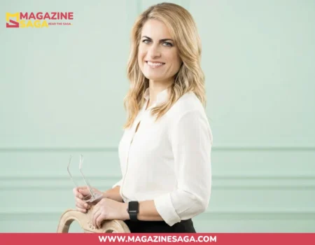 Karen Carney smiling in a white blouse, holding glasses in a professional studio setting