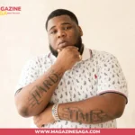 Rod Wave, American rapper, posing in a white patterned polo with "Hard Times" arm tattoos visible.
