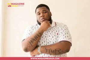 Rod Wave, American rapper, posing in a white patterned polo with "Hard Times" arm tattoos visible.
