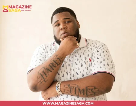 Rod Wave, American rapper, posing in a white patterned polo with "Hard Times" arm tattoos visible.