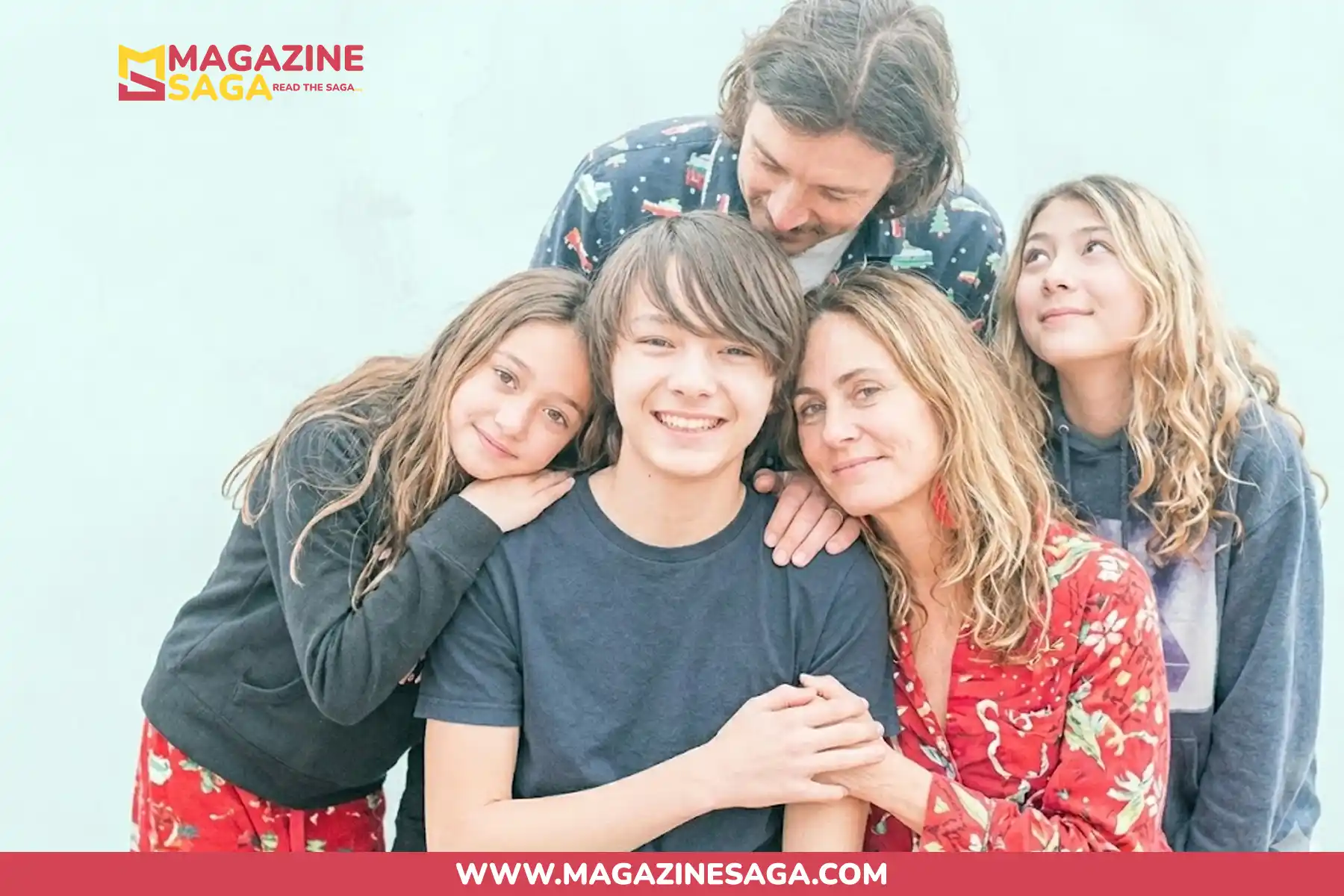 A man and woman pose with three children in a casual family portrait against a light blue background.