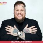 Jelly Roll biography photo, smiling man with face and hand tattoos in black suit