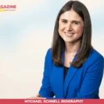 Mychael Schnell biography photo, smiling in blue blazer against neutral backdrop