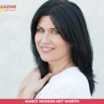 Nancy McKeon net worth portrait, dark-haired woman in white top smiling over shoulder against gray backdrop