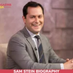 Sam Stein smiling in gray suit and striped tie during TV studio interview