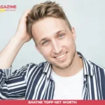 Shayne Topp smiling in striped shirt, hand in hair, studio headshot