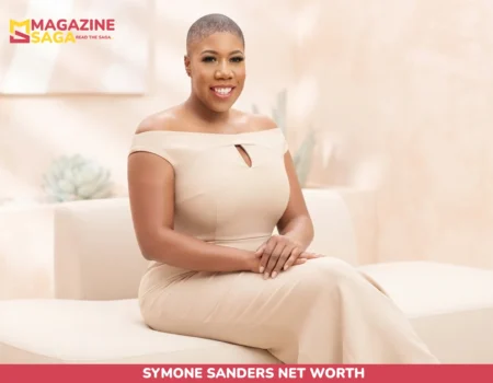 Symone Sanders Net Worth: seated portrait in beige off-shoulder jumpsuit, studio backdrop