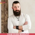 Thane Rivers biography portrait, bearded man in cream sweater with pendant necklace