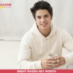 Brent Rivera smiling in cream hoodie holding mug, portrait for net worth article