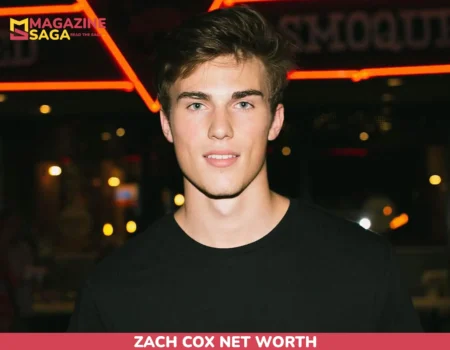 Zach Cox in a black t-shirt at night in front of a red neon sign for the net worth article