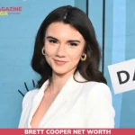Brett Cooper net worth article portrait, smiling in a white blazer against a blue event backdrop.