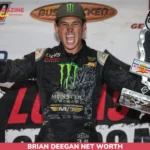 Brian Deegan net worth photo: racer celebrating with trophy and raised fist in a Monster Energy race suit.