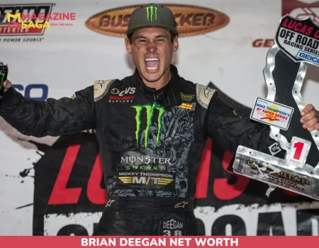 Brian Deegan net worth photo: racer celebrating with trophy and raised fist in a Monster Energy race suit.