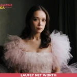 Laufey seated by a window in a pink ruffled tulle gown, portrait for the Laufey net worth article